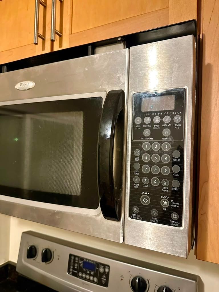 A stainless steel microwave with a grease film across the door and control panel
