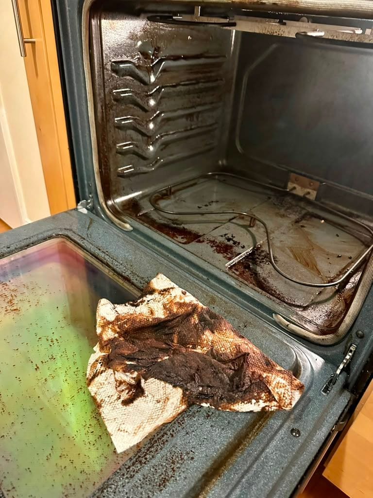 An oven interior with heavy burnt-on residue across the floor and door