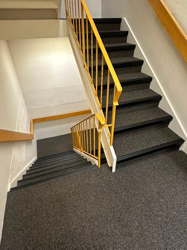 A cleaned stairwell with carpeted treads and a painted handrail in a managed property