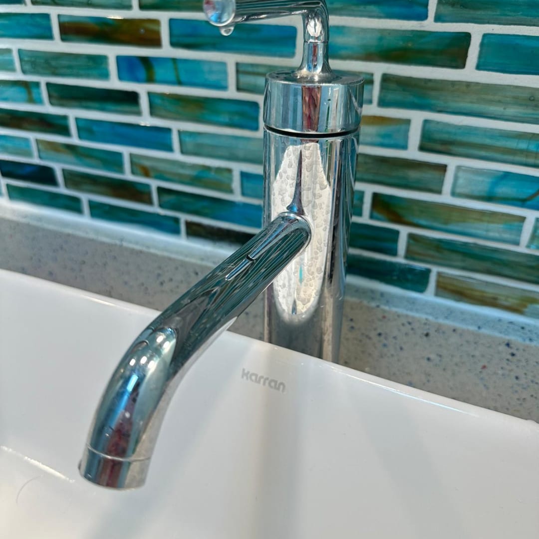 A polished chrome faucet over a bathroom counter with coloured tile