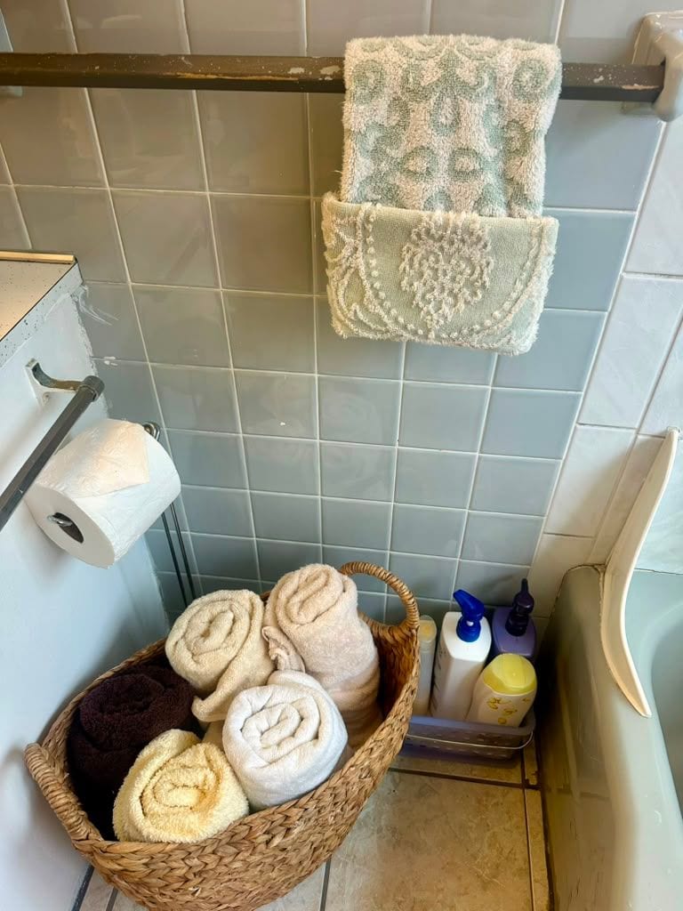 A cleaned bathroom with rolled towels in a basket