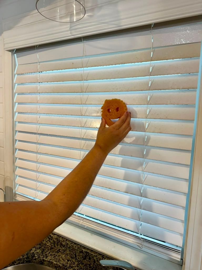 A gloved hand cleaning the slats of a window blind