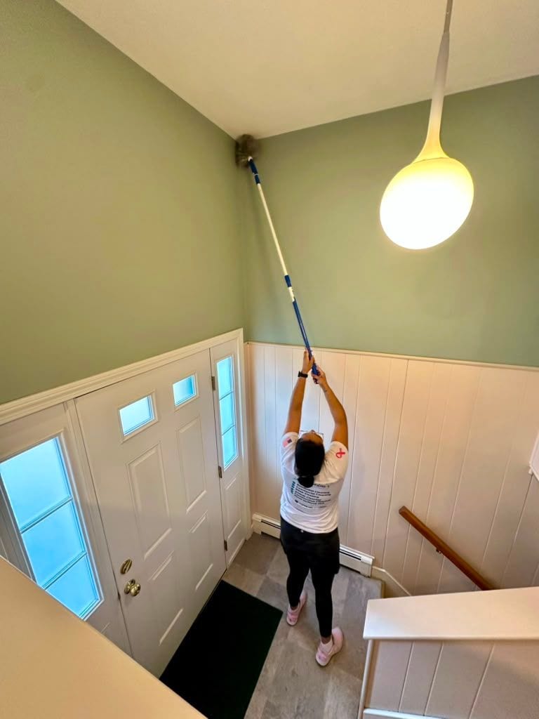 A team member cleaning a ceiling light fixture with an extension pole