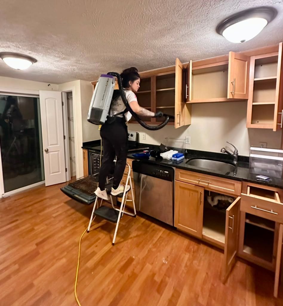 A Cupertino's team member on a step ladder vacuuming inside emptied kitchen cabinets