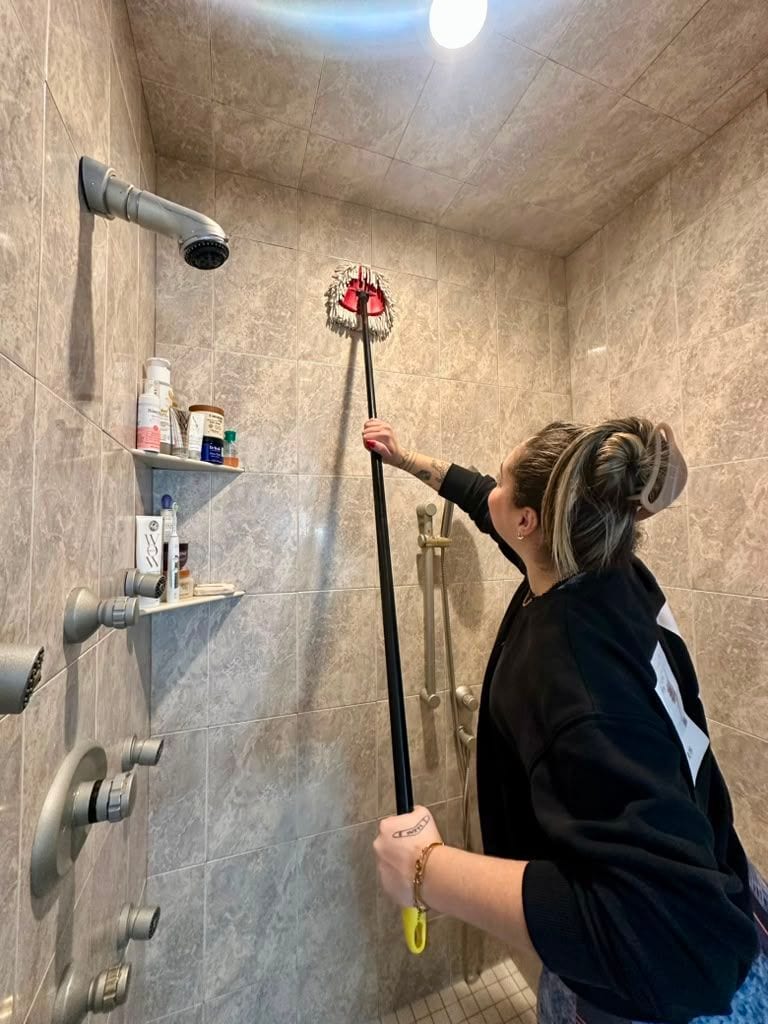 A team member cleaning a shower enclosure with a long-handled tool