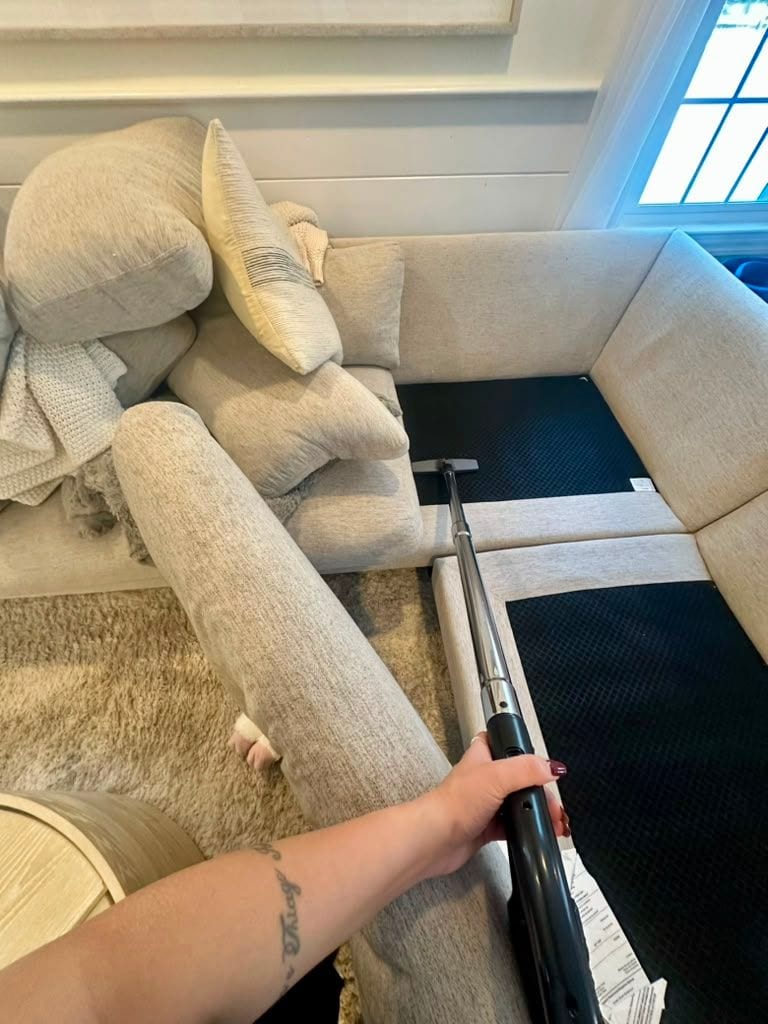 A team member vacuuming a sofa with an upholstery tool